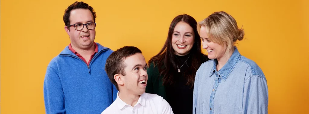 Four people on yellow background looking at each other and smiling