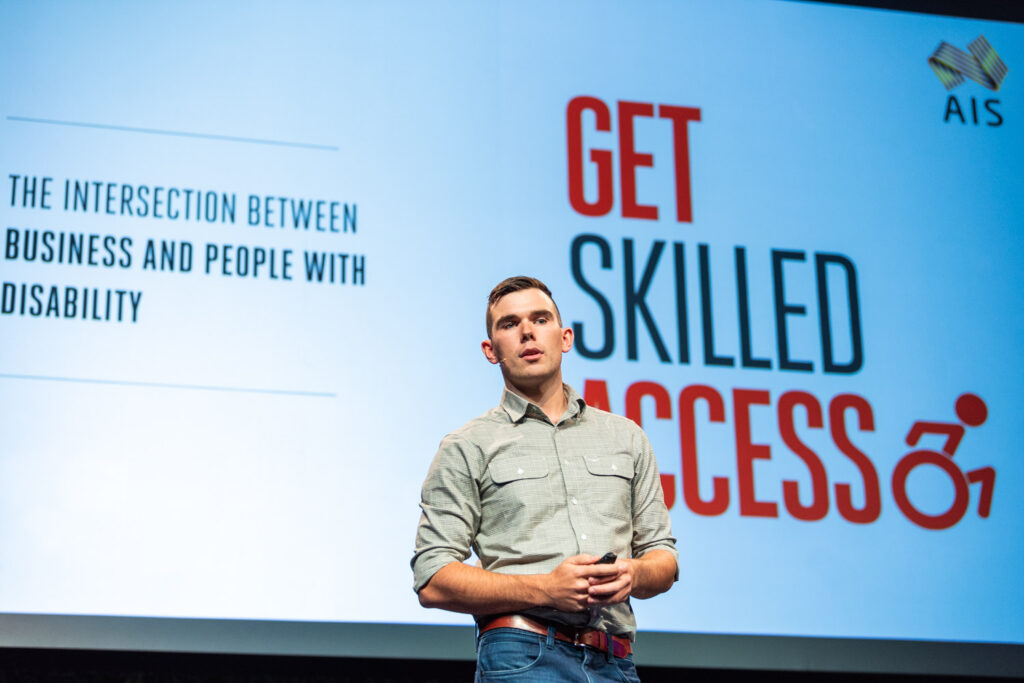 A man with low vision presenting in front of a large screen that says "Get Skilled Access".