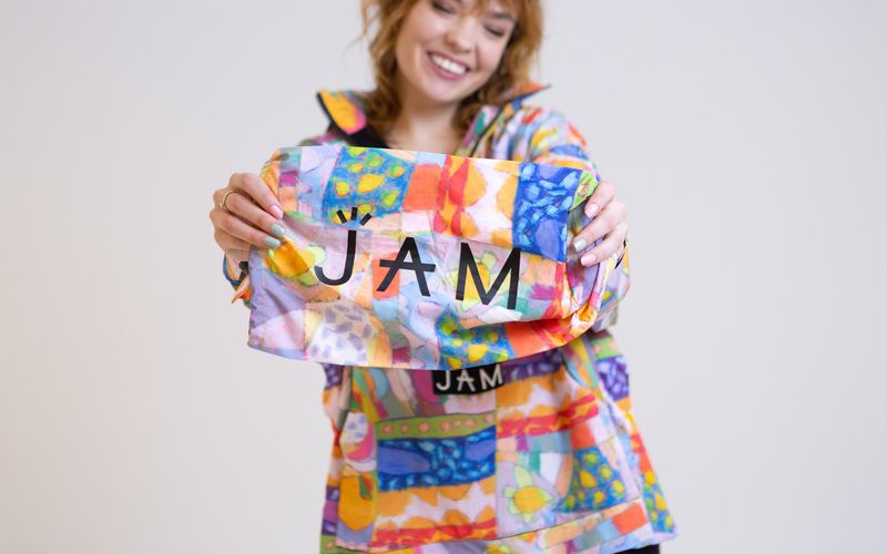 A woman in colourful JAM clothes holding up a matching piece of fabric with the JAM label on it